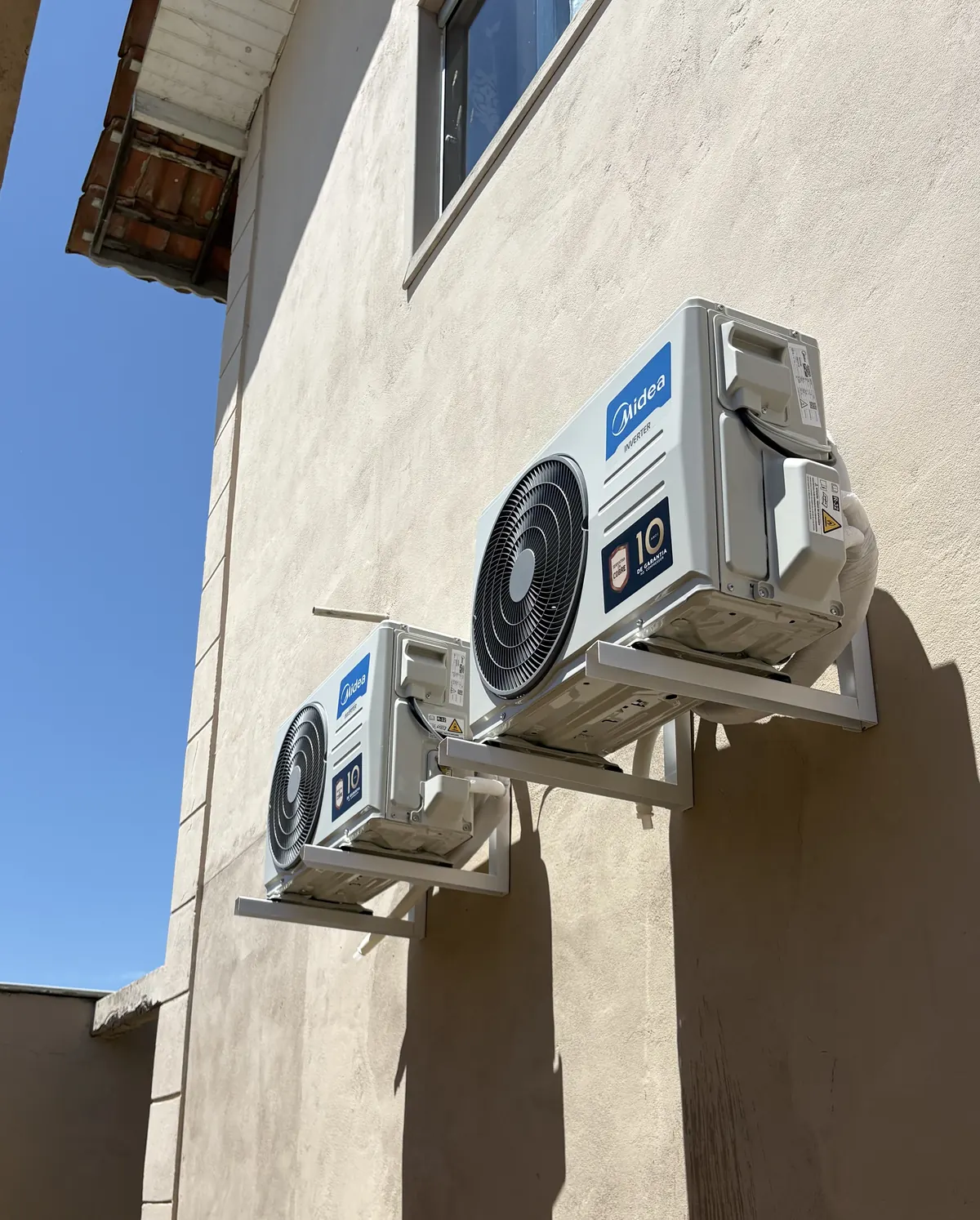 Duas condensadoras Midea instaladas em suportes na fachada de uma casa, sob sol forte